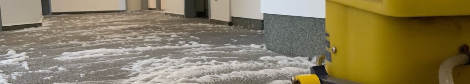Tiefenreinigung von Teppichboden im Objektbereich Eine professionelle Reinigungsmaschine behandelt mit Schaum einen grauen Teppichboden in einem modernen Flur